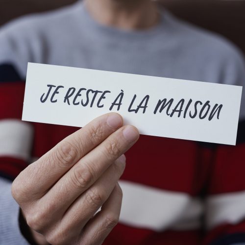 Man Showing The Message I Stay At Home In French closeup of a man, in casual wear indoors, showing the message I stay at home in french written in a piece of paper, as a measure to stop the spreading of the covid-19